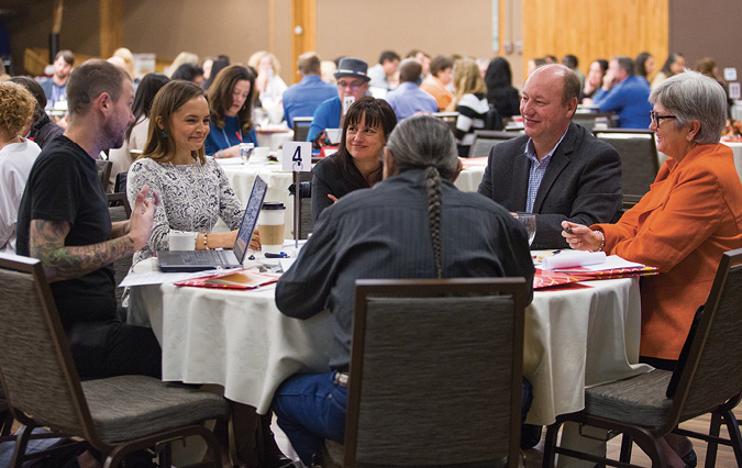 Colour Photograph: Individuals sitting around table in conversation with one another.