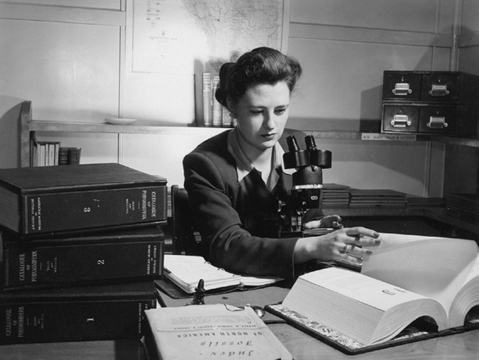 Diane Loranger began her career as a geologist at Royalite, rose to an executive position at Imperial Oil and later became an international consultant on paleontology. In the photo she is wearing a business suit, seated at a desk with a microscope and surrounded by geological texts.