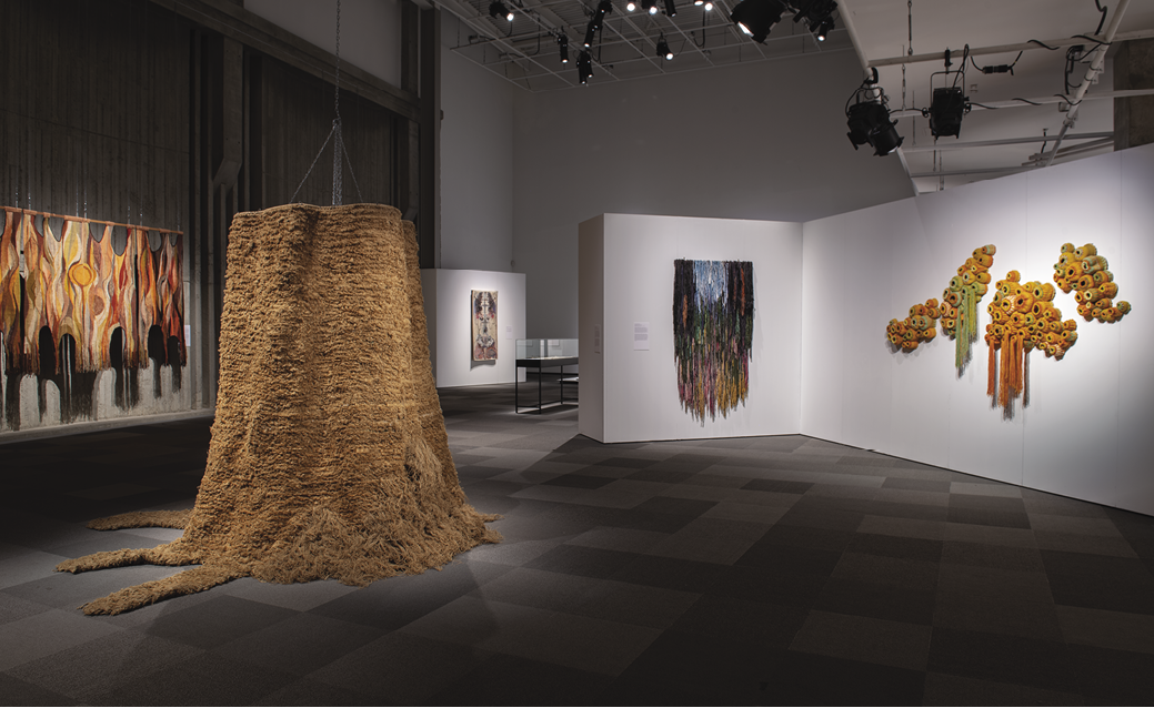 Photo: Wide-lens photo of several pieces in a gallery setting. Light rigging and white walls at angle with the art all under individual spotlights