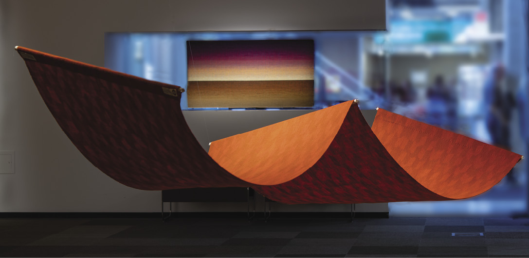 Photo: an orange patterned mat in with a pole in the center so it forms a loose w-shape. Another art is in the background as are fuzzy people and doorways.