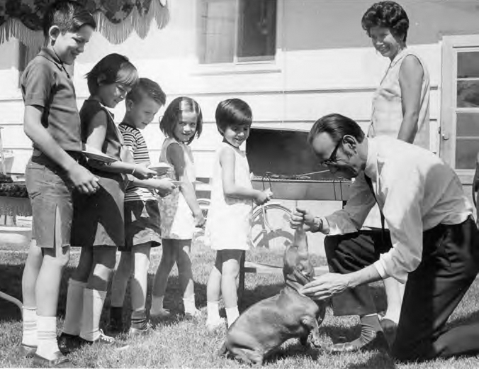 A photograph shows five children, a man playing and feeding a dog. A lady and a building can also be seen.