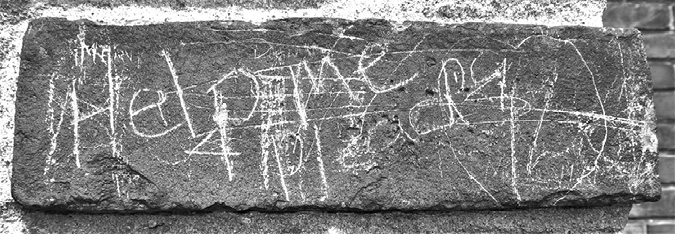Black and white photograph: Single brick with writing that reads “Help me.” The word “Pleads” also appears.