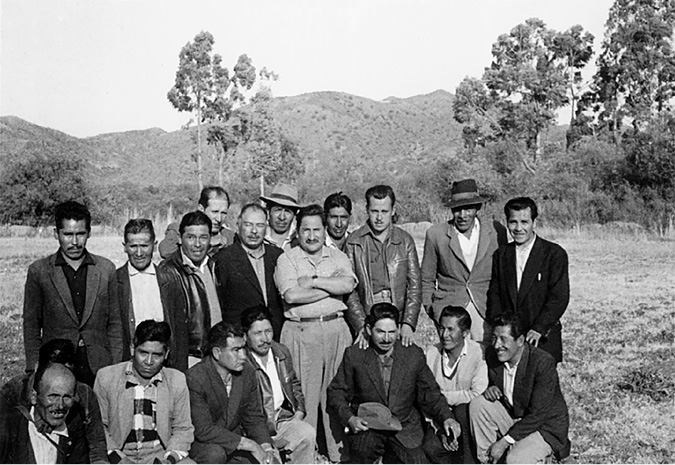 A group of peasant leaders pose for an outdoor photograph in a valley landscape.