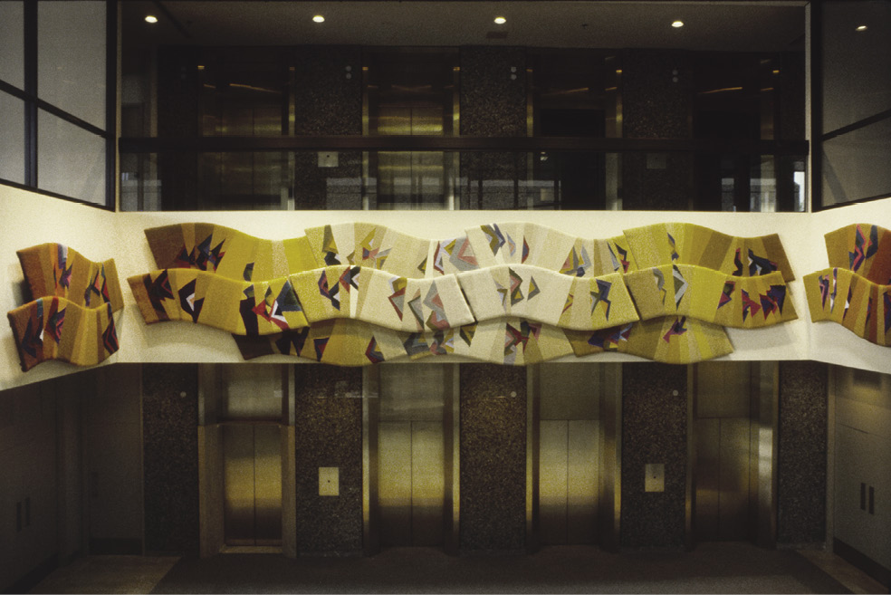 Photo: wavy artwork on three walls inside a high-ceilinged room. The art is tan, yellow, off-white with triangle burst of colour throughout. 