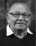 Black and white photograph: Portrait of a man wearing glasses and a collared shirt with a sweater over top. 