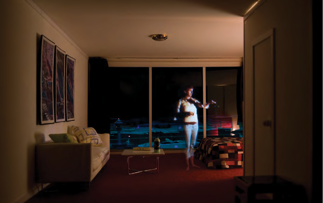 Colour photograph: A diorama of a bedroom in a suburban home, with a projected image of woman on the phone.