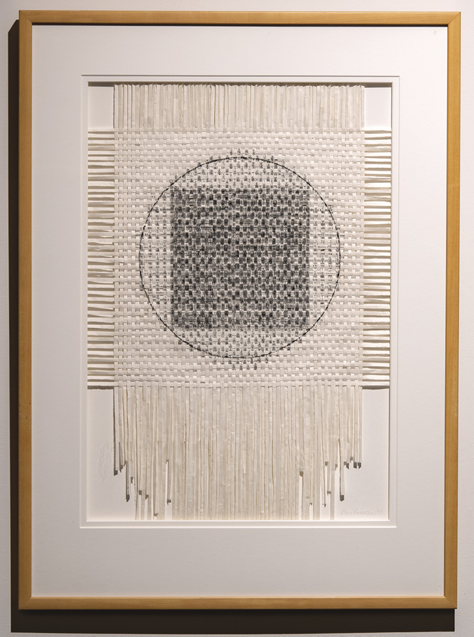 Photo: a mounted and framed series of vertical and horizontal strips of white material woven in the middle and a black circle overlaid on an uneven black square in the middle. 