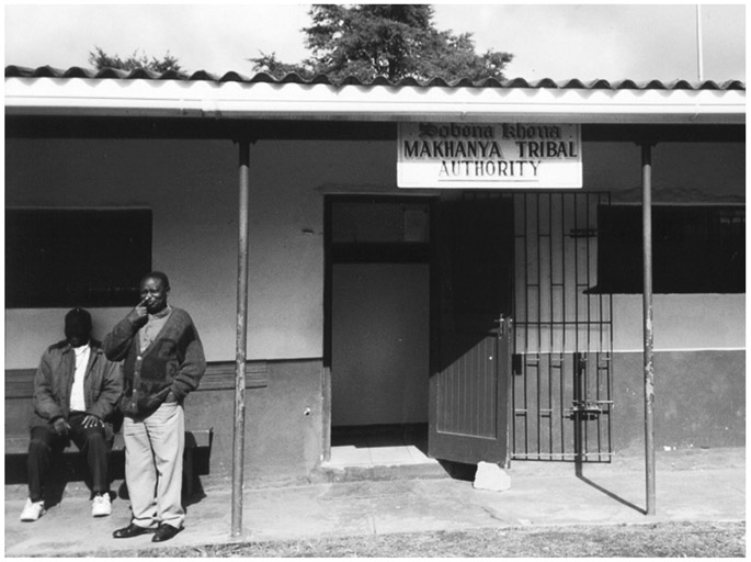 A black and white photograph of Sobonakhona Makhanya Tribal Authority Court. Two people are waiting outside the court.