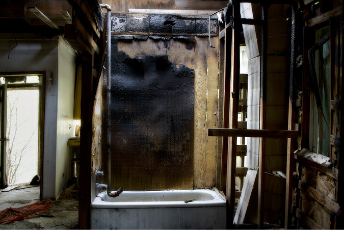 In the centre of an abandoned house, where walls and doors and windows are long demolished, a bathtub with plumbing pipes connecting to nowhere catches the light streaming inside.