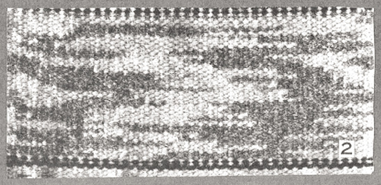 Photo noir et blanc : vue agrandie d’un tissage blanc et gris foncé avec deux lignes noires dans la partie supérieure et inférieure, et le chiffre 2 dans le coin inférieur droit. 
