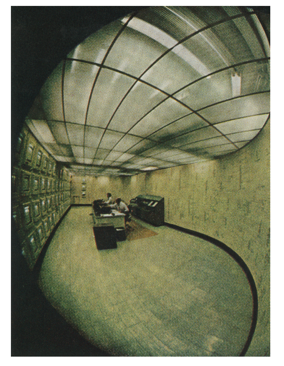 Colour photo collage: The interior of a room with two people working at desks, facing a full wall of monitors, seen through a fish-eye lens.