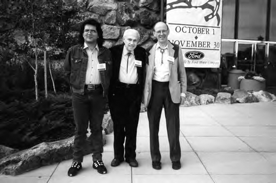 A photograph shows three men wearing formal dresses. A notice board with the text October 1 to November 30 by Ford and trees can be seen in the background.