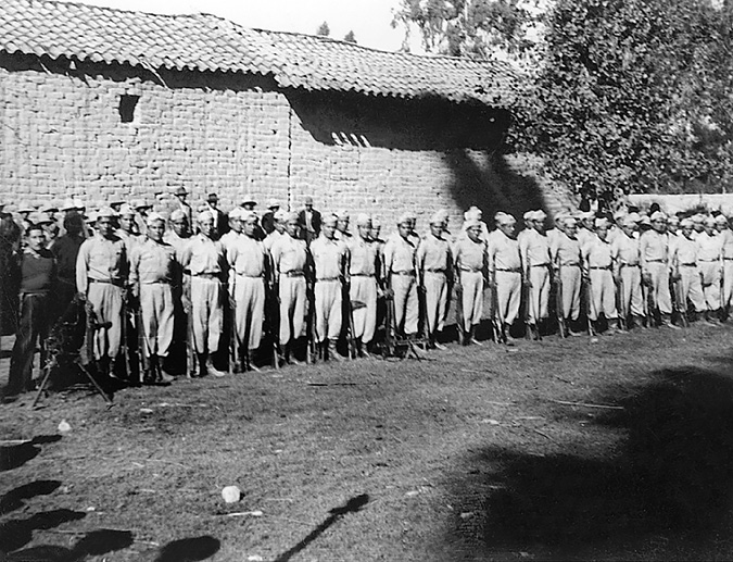 A squad of militiamen in uniform pose armed in a peasant barrack.