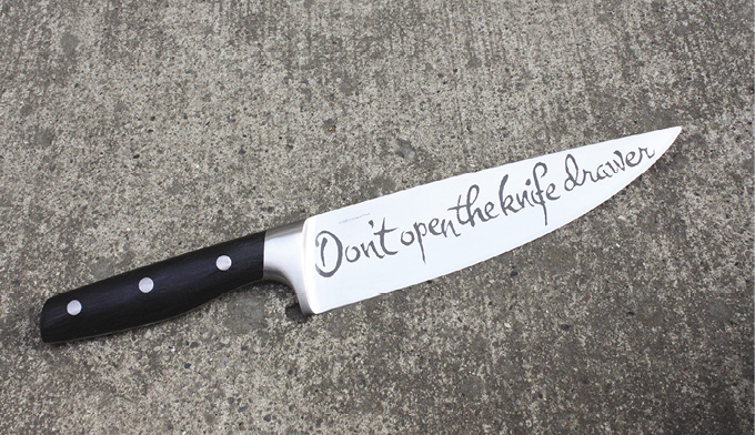 Photo: a butcher knife on a cement floor with handwriting font on the blade reading “Don't open the knife drawer.”