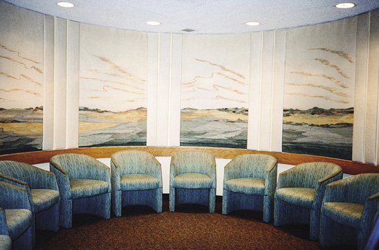 Photo: Ten blue club chairs sit in a semi-circle between some similar wall hangings of green field with hills in the background.