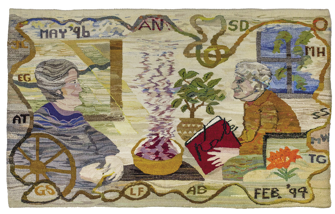 Photo: horizontal piece featuring two people looking at wone another while seating with a bowl of something pink and steaming between them. One person holds a red book with the word “Kate” on it. A swirly thread border holds a series of initials: EG, AT, GS, LF, AB, TG, MW, SS, MH, SD, AN. There are two dates: May ’96 in the top left, and Feb. ’94 in the bottom right.