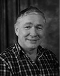 Black and white photograph: Portrait of a man smiling and wearing a plaid shirt.