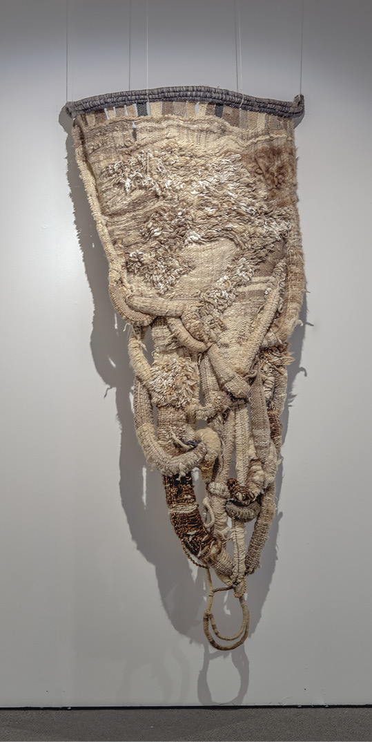 Photo: a pizza shaped hanging pointing down. It is in shades of tan and brown with big loops of fabric created a 3d effect.