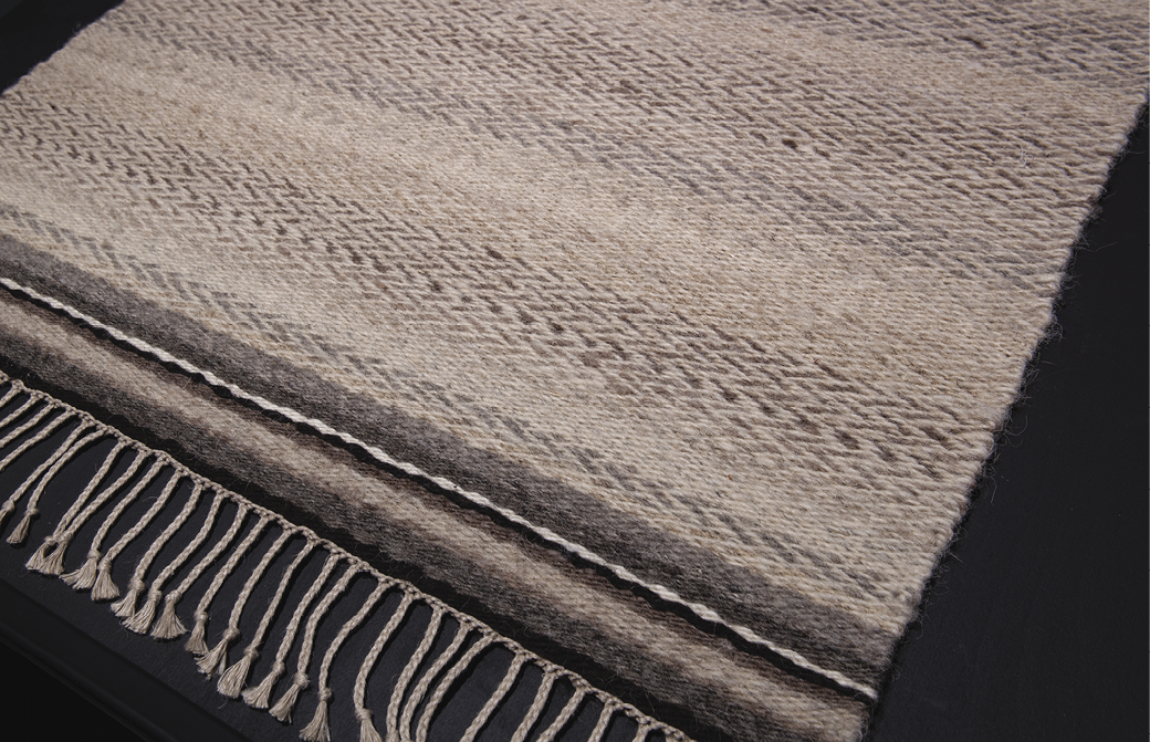 Photo: close-up on a woven rug in greys and browns with a fringe.