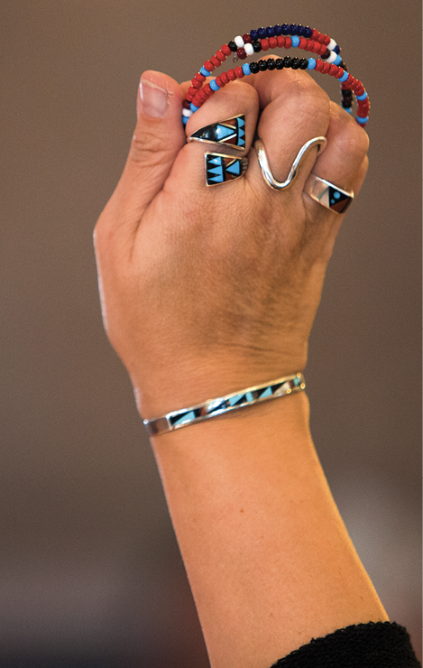 Colour Photograph: Individual’s hand poised in the air, holding colourful beaded bracelets