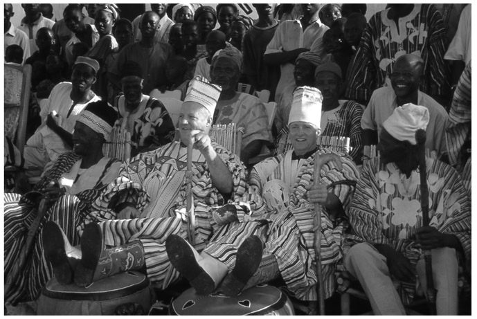 A black and white photograph of newly enskinned Canadian development chiefs of the Wechiau Hippo Sanctuary, Alex Graham and Brian Keating, with the audience behind them.