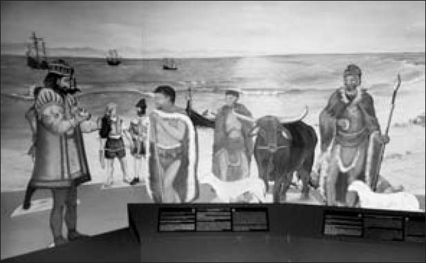 A painting of a few men in grand attire speaking to a couple of cattle herders by the beach. Three ships are visible in the distance.