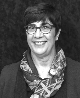 Black and white photograph: Portrait of woman with a short black hair and glasses, wearing a scarf. She is looking at the camera and smiling.