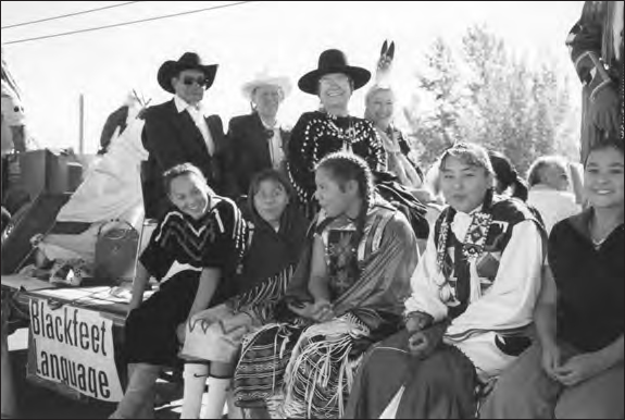  A photograph shows a group of people sitting in a vehicle with the text Blackfeet Language. Trees can be seen in the background.