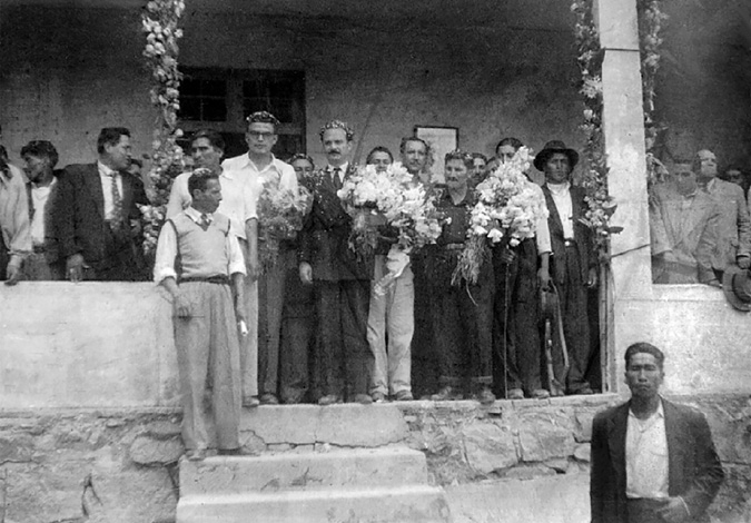 Government and union officials, holding bouquets in their hands, pose at the entrance of a peasant union office, surrounded by civilians and armed militiamen.