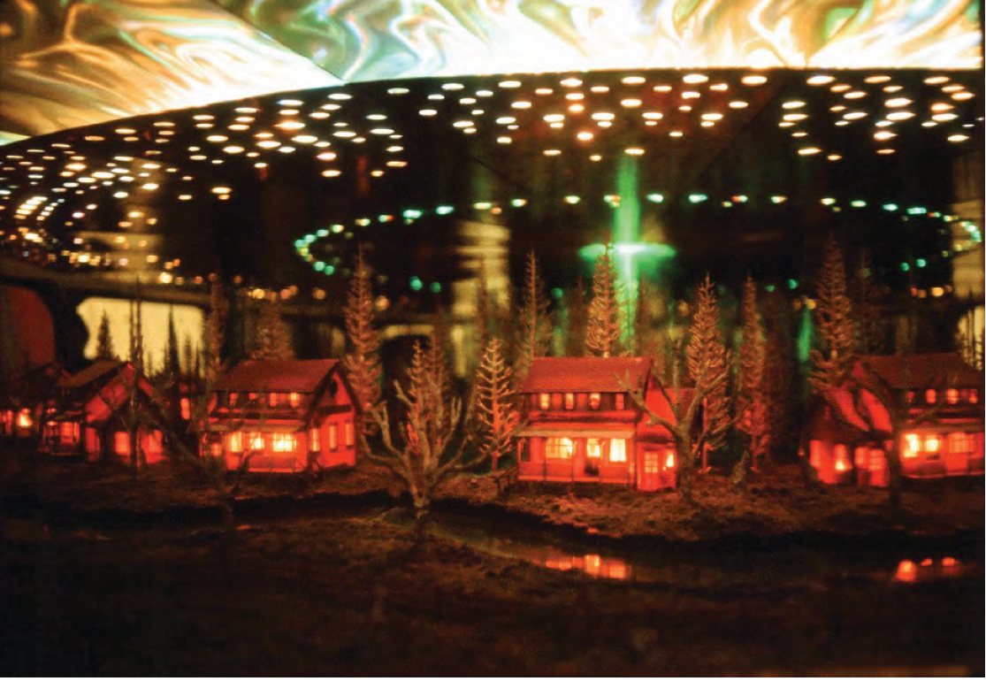 Colour photograph: A diorama showing a huge spaceship hovering over four large houses.