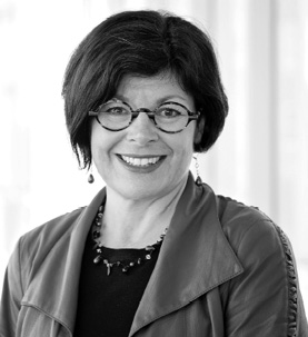 Black and white photograph: A portrait of a woman with short black hair, wearing stylish round glasses and a jacket. She is looking directly at the camera, smiling.