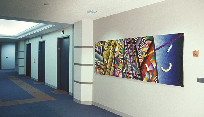 Photo: a long horizontal art mounted on a white wall in a hallway near the elevators. It is many coloured with black-and-white checkerboard flashes.