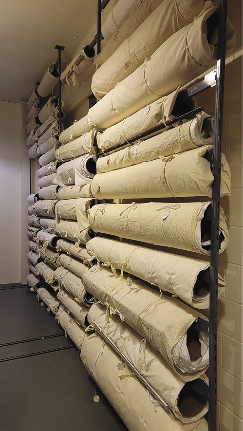 Photo: Several linen-wrapped tubes hang on a wall in four columns on a cinder block wall.