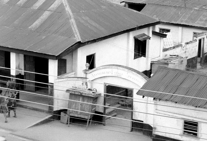 A black and white photograph of white houses with a slanting roof of the former Asante King’s police station in Kumasi having a small gate-like entrance.