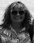 Black and white photograph: Photograph of a woman in sunglasses and a patterned shirt outside with the sun shining on her. 