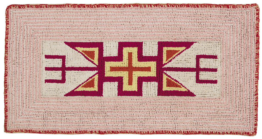 Horizontal rug with alternating pink and white lines surrounding a red-yellow-dark pink cross inside of a white rectangle in the center with two similarly coloured triangles on each side and dark pink forks coming out of the center. The whole thing is outlined in red.