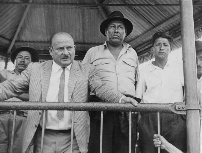 A man delivers a speech from a gazebo of a rural town plaza, while peasant leaders at his back listen attentively.