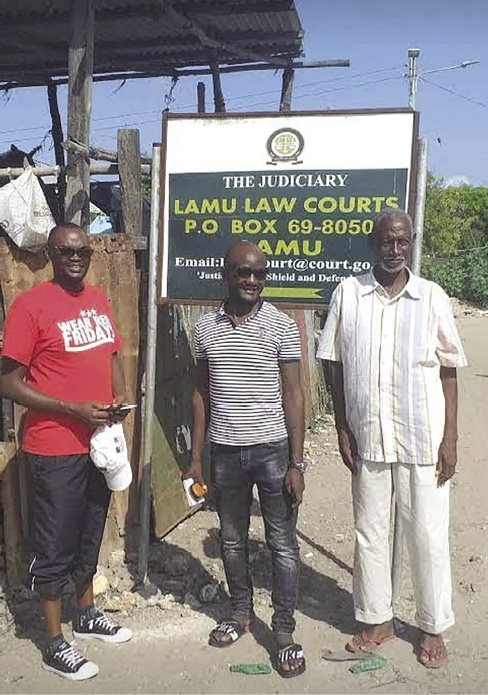 Colour photograph: Photo of three male activists next to a Lamu Law Courts sign.