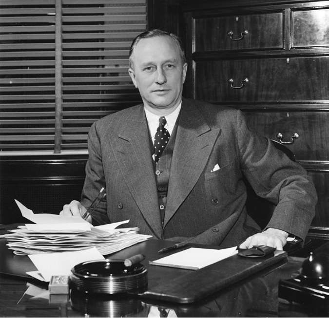 Hewetson was president (and later Board Chair) for Imperial Oil during the Leduc era. The photo shows him behind a desk (laden with papers), a cigar in an astray. He wears a three piece suit and gazes directly at the camera, possibly emulating his predecessor Walter Teagle, who he resembles physically.