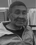 Black and white photograph: Portrait of a man outside wearing a zip-up light jacket and a t-shirt.