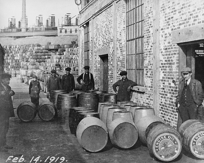 The Dartmouth refinery (also called Imperoyal) was one of several new refineries constructed under Teagle between 1915 and 1918. In this photo a group of yard workers pose outside a brick warehouse surrounded by oil cans marked “Engine Oil.” 