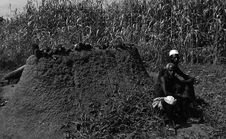 Two men sit beside a tall mound of sand in a field.