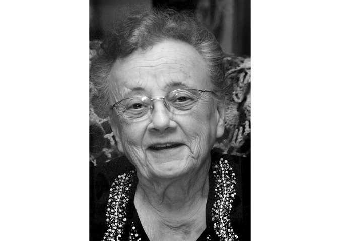 Black and white photograph. Head and shoulders portrait of an older woman. She is wearing glasses, and a beaded black blouse.
