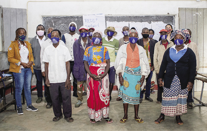 Colour photograph: Photo of 18 people, women and men, standing in a schoolroom in front of a blackboard.  All wear Covid masks.