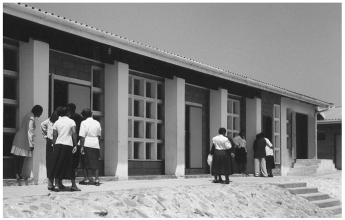 A black and white photograph of KwaXimba Administration Offices which is a meeting place for Ward Councillors and Izinduna. Several ladies in shirts and men in shirts and trousers are seen gathered outside the office.