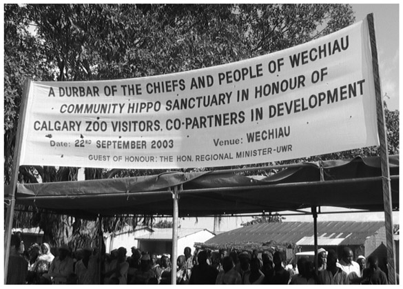 A black and white photograph of the banner hung high over a canopy, with text A Durbar of the chiefs and people of Wechiau Community Hippo Sanctuary in honour of Calgary Zoo Visitors, co-partners in development.