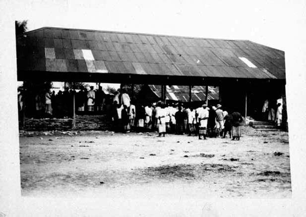 A black and white photograph shows villagers gathered in front of a destroyed courthouse.